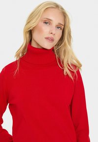Rdeči pulover s turtle neck iz rebraste tkanine, z visokim ovratnikom in dolgimi rokavi, gladke teksture in prileganja.