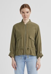 Olivenfarbene, leichte Jacke mit Stehkragen, vorne mit Reißverschluss, zwei Brusttaschen, Zugband in der Taille und Knopfdetails an den Manschetten.