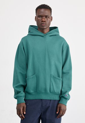 Zielona bluza z kapturem, wykonana z miękkiego materiału. Posiada przednią kieszeń, ściągacze przy mankietach oraz logo na lewym rękawie. Luźny krój.