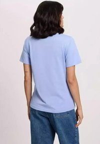 Jasnoniebieska bawełniana koszulka z okrągłym dekoltem i krótkimi rękawami, charakteryzująca się luźnym krojem i gładką fakturą, noszona z niebieskimi dżinsami.
