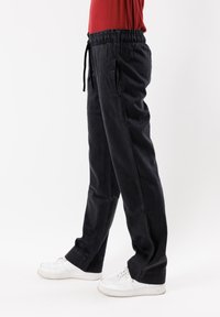 Pantaloni neri, larghi e comodi, realizzati in morbido materiale con vita elastica, tasche laterali e cordoncino. Indossati con sneaker bianche.