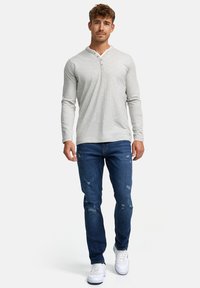 Camisa henley de manga larga gris claro con escote abotonado, combinada con jeans oscuros desgastados y zapatillas blancas.