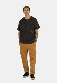 Black textured short-sleeve shirt with chest pocket, paired with light brown corduroy cargo pants, featuring side pockets and black shoes.