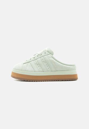 Jasnozielony zamszowy sneaker typu slip-on z sznurowanym przodem, trzema bocznymi paskami i grubą białą oraz brązową podeszwą.