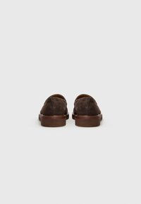 Pair of dark brown suede slip-on shoes with wooden soles, viewed from the back on a plain light background.
