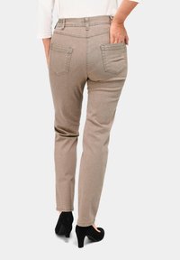 Beige schmal geschnittene Hose aus strukturiertem Stoff mit zwei Gesäßtaschen, kombiniert mit schwarzen hohen Schuhen.