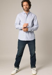 Lichtblauw languit shirt met kleine witte stippen, met een knoopsluiting bij de kraag, gedragen met donkerblauwe jeans en witte sneakers. Casual pasvorm.