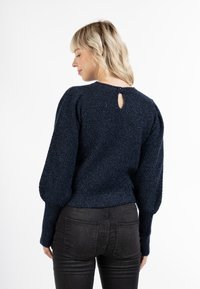 Sötétkék kötött pulóver, texturált felülettel, puffos ujjakkal és egy kis kulcslyukkal a háton. Rugalmas szegély és mandzsetta.