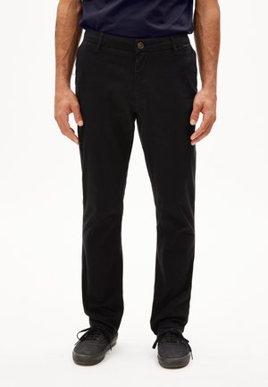 Black chinos made from cotton, featuring a straight cut, button closure, side pockets, and a smooth texture. Worn with dark shoes.