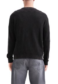 Pull en tricot noir avec un tissu texturé, col rond et poignets côtelés. Assorti à un jean texturé gris clair.