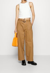 Beskurad vit linne, beige vida byxor med en silver spänne, svarta skor och en liten orange handväska.