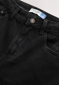 Høj talje, vide sorte denimjeans med kobberdetaljer, fem lommer og en mærkat med teksten "WIDE LEG HIGH RISE." Glat tekstur.