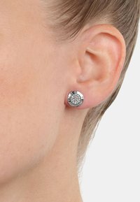 Orecchini a chiodo in argento con design circolare, caratterizzati da un centro testurizzato e accenti incisi lungo il bordo. Finitura liscia e aspetto lucido.