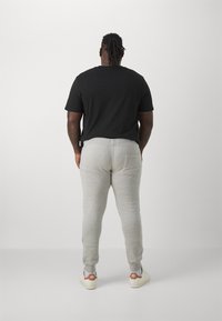 Herreantrekk bestående av en svart bomull t-skjorte og lysegrå joggebukser med baklomme, iført hvite joggesko med røde detaljer.