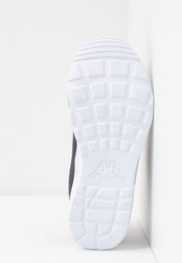 Černá atletická podrážka s texturovanou bílou podrážkou, která má charakteristický vzor špice a jemné logo poblíž paty.