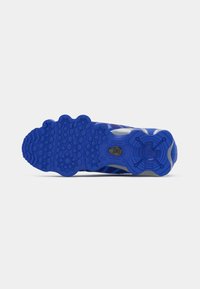 Semelle de chaussure de sport bleue avec des motifs en caoutchouc texturé, comportant des grips circulaires et hexagonaux ainsi qu'une indentation centrale pour la stabilité.