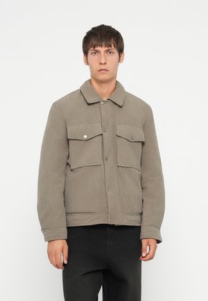 Chaqueta de pana gris con cuello, dos bolsillos frontales y cierres de botón. Complementada por un diseño texturizado y estructurado.