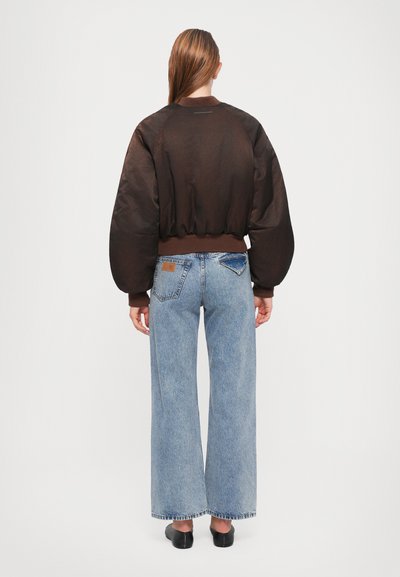 Brown, semi-sheer bomber jacket with puffed sleeves and ribbed cuffs, paired with wide-leg blue denim jeans featuring a patch pocket.