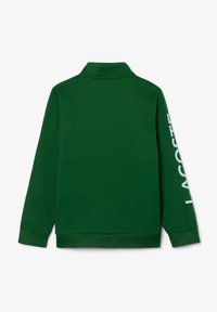Zelena dolgoročna polosrajca, narejena iz mehke tkanine, z zavihanim ovratnikom in z besedo "LACOSTE" v beli barvi na desnem rokavu.