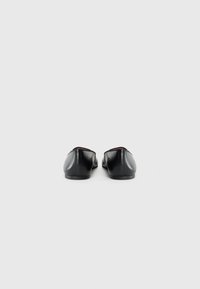 Chaussures plates en cuir noir avec un bout rond, un design sans coutures et des détails minimalistes, caractérisées par un profil bas et une texture lisse.