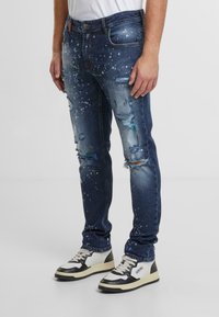 Slim-fit blå jeans med slitna detaljer, sprayfärgsaccent och fransiga fållar. Tillsammans med vita och svarta högskor.