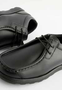 Chaussures noires en cuir avec un bout rond, texture lisse et coutures décoratives. Présentent un design à lacets et une semelle en caoutchouc pour plus d'adhérence.