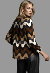 Langärmlige Bluse mit Wellenmuster in Dunkelbraun, Hellbraun, Creme und Schwarz. Hergestellt aus glattem Stoff mit entspannter Passform.
