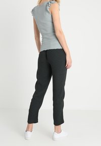 Jasnoniebieska ribkowana bluzka z falbankami na rękawach, połączona z czarnymi spodniami w kropki i białymi trampkami, widok z tyłu.