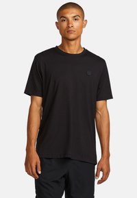 Schwarzes T-Shirt mit kurzen Ärmeln, aus weichem Stoff, mit einem runden Halsausschnitt und einem kleinen runden Logo auf der linken Brustseite.