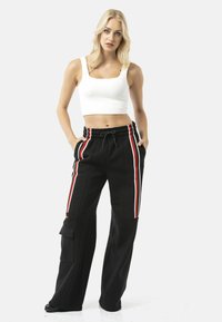 Zwarte sweatpants met rode en witte strepen, een cargozak en een elastische tailleband. Gecombineerd met een nauwsluitend wit cropped topje.