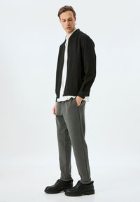Sort zip-up bomberjakke over en hvid skjorte, parret med grå sweatpants og sorte snørebåndsstøvler. Glat stof, moderne snit, afslappet pasform.