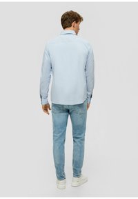 Camicetta a maniche lunghe azzurra chiara con colletto, polsini con bottoni e orlo dritto, abbinata a jeans in denim chiaro e sneaker bianche.