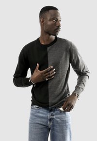 Maglione a blocchi di colore nero e grigio con collo rotondo, maniche lunghe e texture liscia, abbinato a jeans in denim azzurro chiaro.