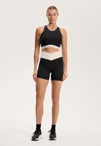 Črn športni crop top z kontrastnim belim trakom; v kombinaciji s črnimi visokimi hlačami z belo črto v obliki vijačnice.