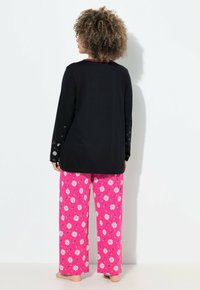 Černý dlouhý rukáv top s barevnými vzorovanými rukávy, doplněný o růžové široké kalhoty s bílými květinovými motivy. Měkká tkanina, uvolněný střih.