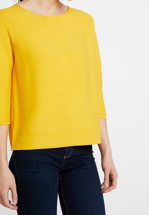 Gelbes, leichtes Strickoberteil mit Dreiviertelärmel, Rundhalsausschnitt und geripptem Saum. Tragen mit dunklen Jeans. Glatte Textur.