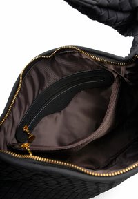 Borsa nera in pelle intrecciata con un interno liscio di colore marrone scuro, dotata di una tasca con zip e dettagli in metallo dorato. Chiusura con zip sulla parte superiore.