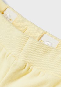 Cintura acanalada amarilla con cierre de botón, textura de tela suave, volantes en la parte inferior y un patrón de rayas vertical cerca de la parte superior.
