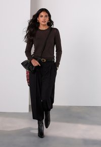 Brun top med lange ærmer kombineret med sorte bukser med høj talje. Sort håndtaske, spidse læderankelstøvler og simple guldsmykker.