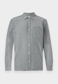 Camisa de botones gris hecha de una tela ligera. Presenta un bolsillo en el pecho y un pequeño logotipo. Cuello clásico y manga larga.