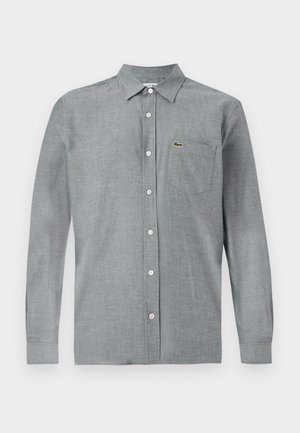 Camicia grigia con bottoni realizzata in un tessuto leggero. Presenta una tasca sul petto e un piccolo logo. Colletto classico e maniche lunghe.
