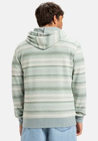 Sudadera con capucha a rayas verdes y blancas. Hecha de material suave, cuenta con un bolsillo estilo canguro y puños de canalé con un ajuste estándar.
