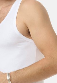 Vit linne med en figurnära design, bomullstyg, slät textur och en öppen halsringning, prydd med ett handledsarmband.