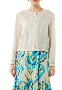 Jasno beżowa kurtka z długimi rękawami, dwiema przednimi kieszeniami, elastycznym dołem, zestawiona z sukienką warstwową w odważne niebieskie i zielone kwiatowe wzory.