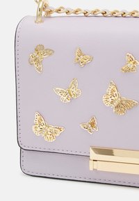 Borsa a tracolla in pelle viola decorata con applicazioni di farfalle dorate e una chiusura dorata. Presenta una superficie testurizzata e una maniglia a catena.