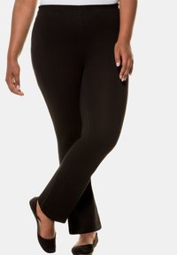 Leggings neri a zampa d'elefante realizzati in un tessuto elastico. Texture liscia con un elastico in vita e una silhouette aderente, abbinati a delle scarpe basse nere.