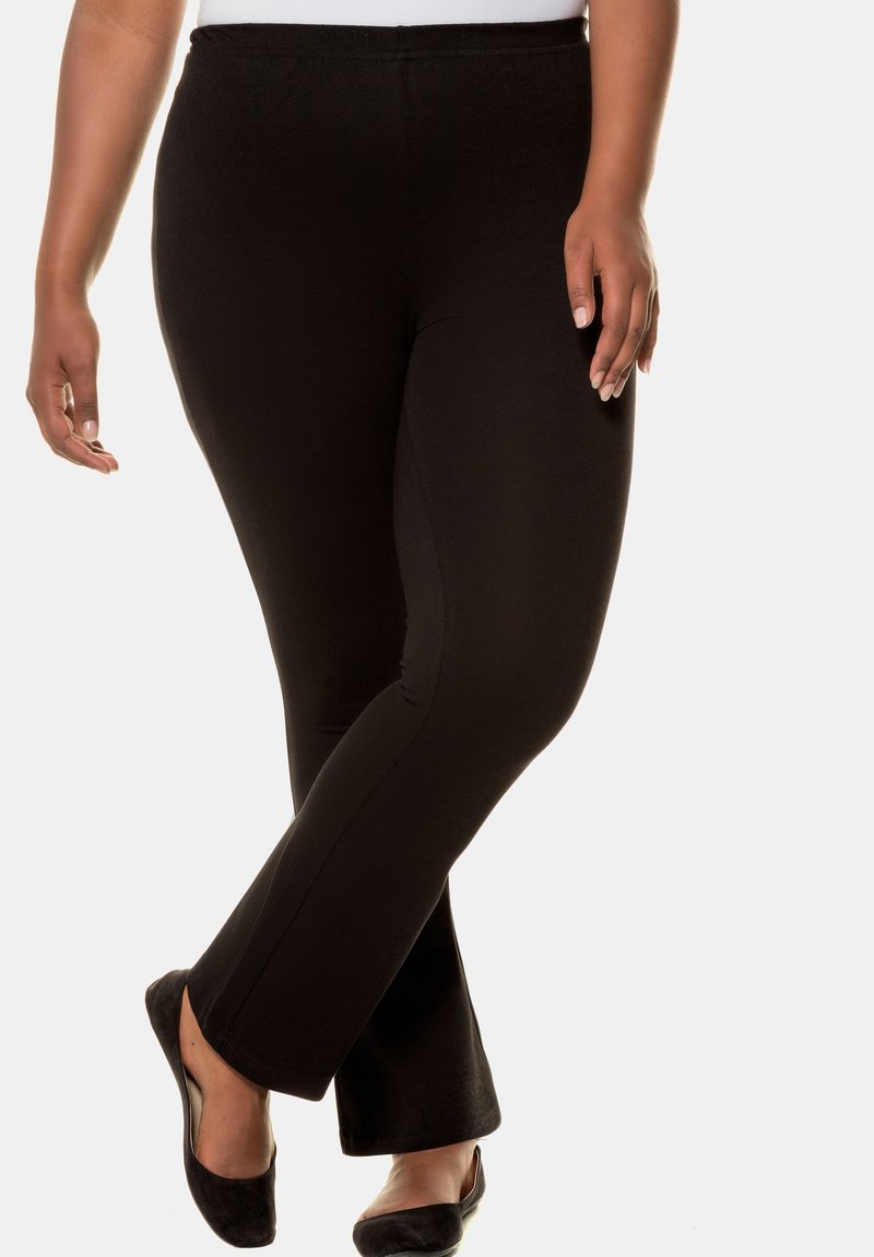 Leggings neri a zampa d'elefante realizzati in un tessuto elastico. Texture liscia con un elastico in vita e una silhouette aderente, abbinati a delle scarpe basse nere.