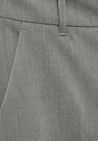 Tissu gris montrant un gros plan de matériau texturé avec un motif chevron subtil, mettant en avant une taille cousue et des détails de poches latérales.