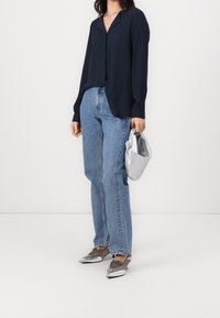 Blusa a maniche lunghe navy, orlo asimmetrico, abbinata a jeans in denim larghi. Scarpe metalliche argento e una piccola borsa lucida argento completano il look.