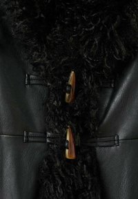 Îmbrăcăminte din piele neagră, cu un tiv texturat, fuzzy, negru, prins cu două butoane decorative, unul chihlimbar și unul negru.